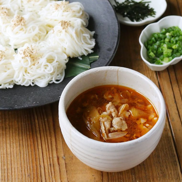 黒皿に盛り付けたそうめんと白い器に入ったねぎ豚だれ