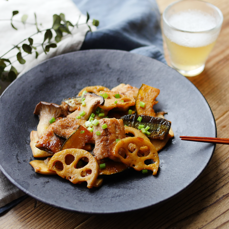 黒い丸皿にさんまとれんこんのにんにく醤油炒めが盛られている