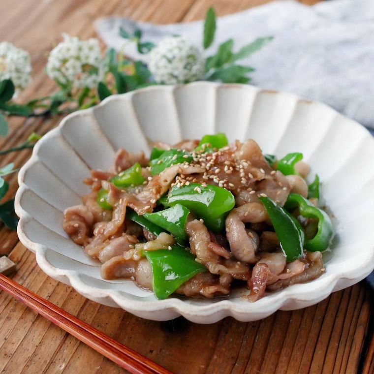 白い花型の皿に豚バラピーマンの甘辛にんにく炒めが盛られている