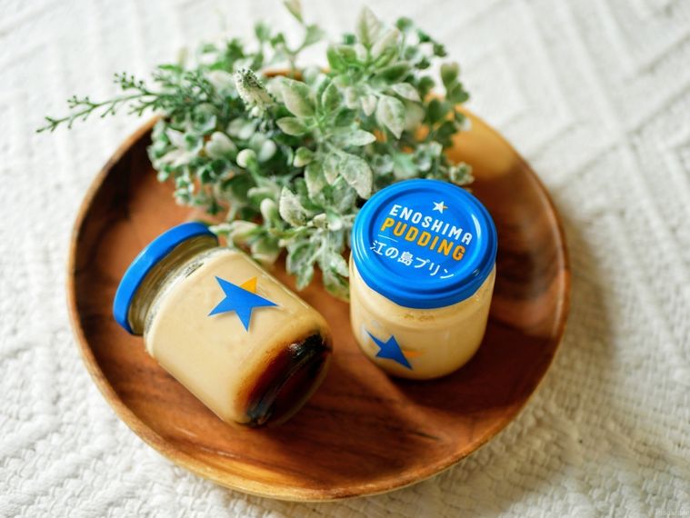 ENOSHIMA PUDDINGと書かれた青いフタつきの瓶に入ったプリンが2つ木の皿にのっている様子
