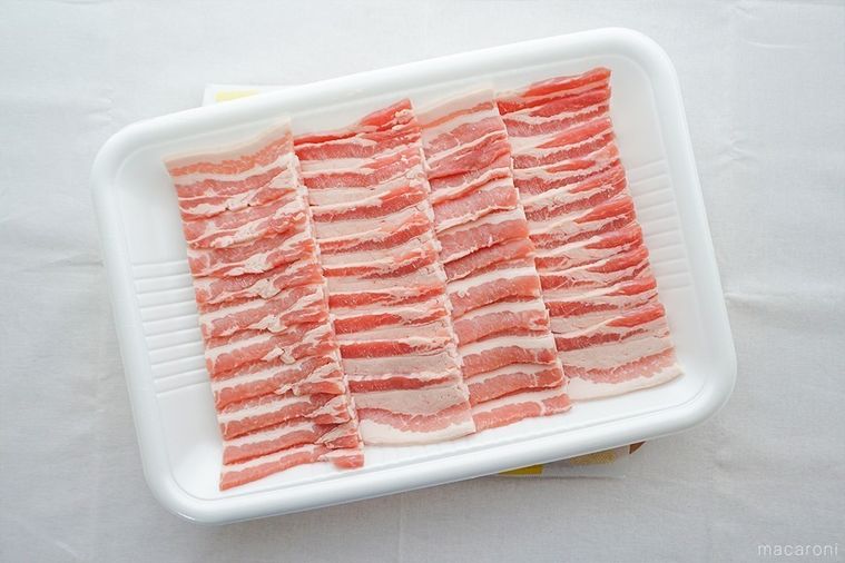 豚バラ肉の入ったトレーを、木のまな板にのせた様子