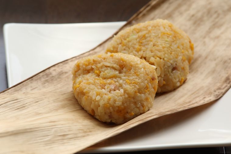 白い四角形の皿と笹の葉の上にのった、おにぎり型の中華ちまき