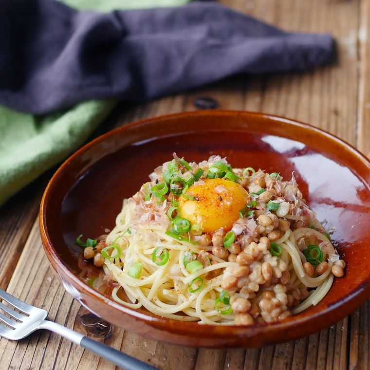 茶色い皿に盛り付けられた納豆とネギの和風パスタ