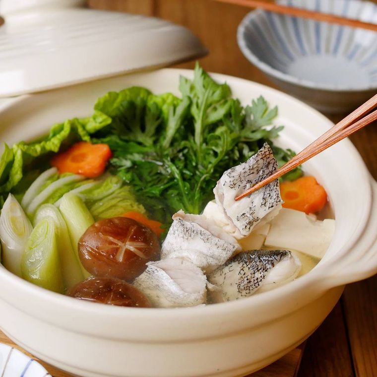 たらちり鍋が入った土鍋、たらを箸でつまんでいる