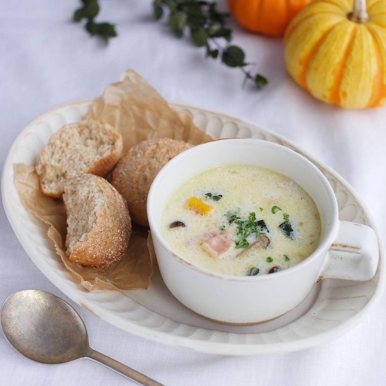 白い器に盛り付けられたかぼちゃとミックスビーンズのスープにパンが添えられている