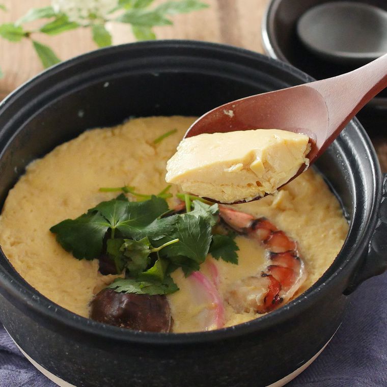 黒い土鍋に入っている茶碗蒸しを木のれんげですくっている