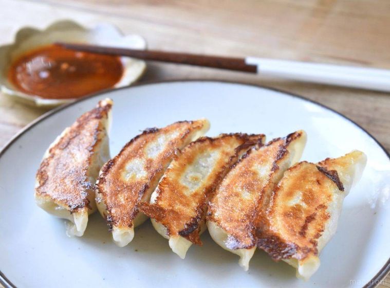 白い丸皿に盛り付けられた焼き餃子に、小皿に入ったタレと箸が添えられている様子