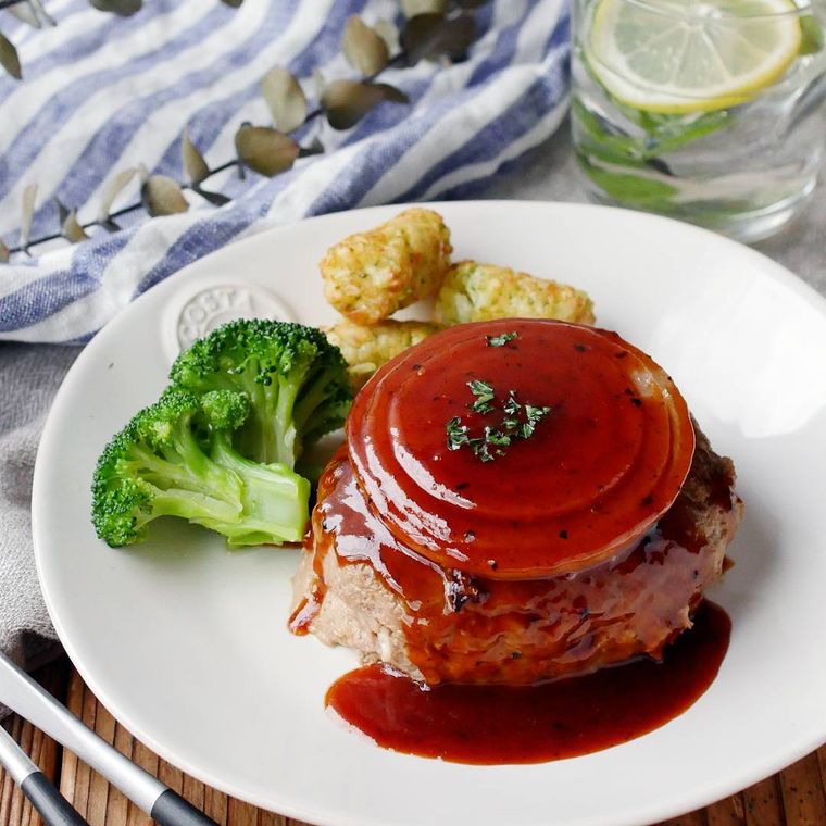 白い皿に盛られたハンバーグにオニオンスライスがのっており、ブロッコリーとハッシュドポテトが添えられている様子