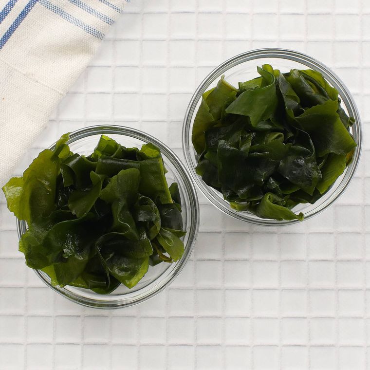水で戻したわかめが2個のガラス容器に入れられており、その横には青いストライプ模様のキッチンクロスが置かれている