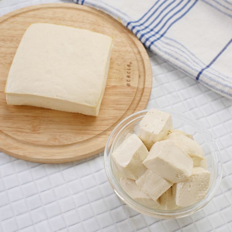 丸い木のまな板の上に木綿豆腐が一丁置かれ、その横にはガラスの器に入った角切り豆腐と、キッチンクロスが置かれている