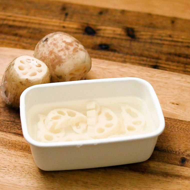 半月切りのれんこんが、白いホーロー容器の中で水にさらされている