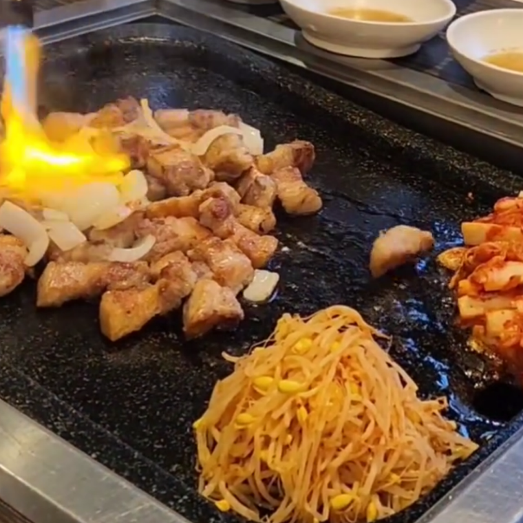 サムギョプサルに付け合わせの野菜を鉄板に並べ、直火でファイヤーしている様子