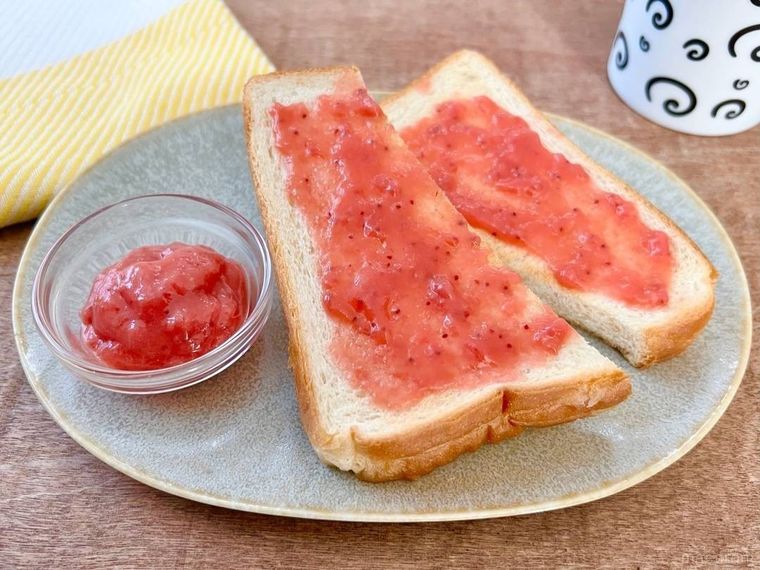 グレーの皿の上に、いちごバターが塗られた食パンが置かれ、その奥には黄色い布巾と、白いマグカップが置かれている