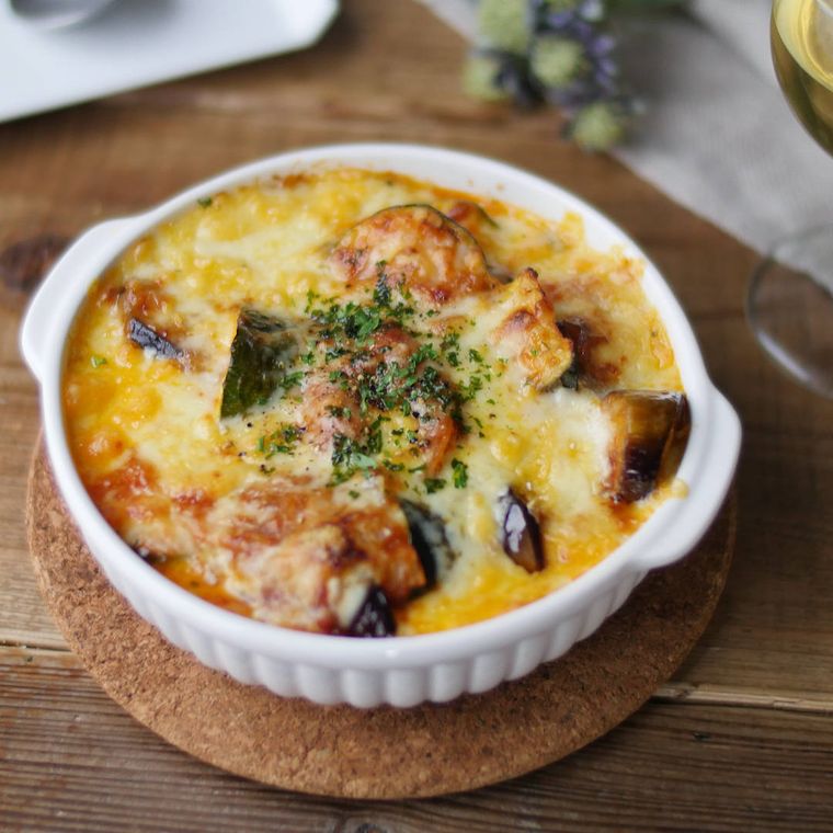 鍋敷きの上の白いグラタン皿に盛られたなすとズッキーニのチリグラタン