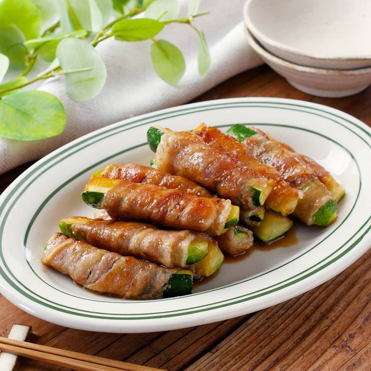 緑のラインが入っている白い楕円形の皿に盛られたズッキーニの肉巻き