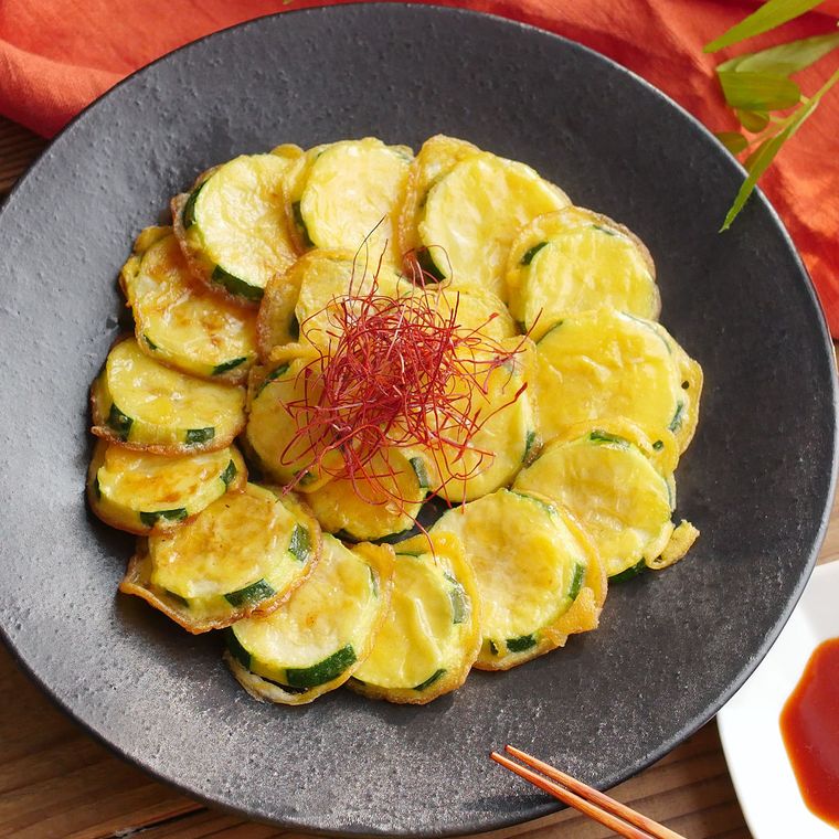 黒い丸い大皿に盛られたズッキーニのひと口チヂミと糸唐辛子