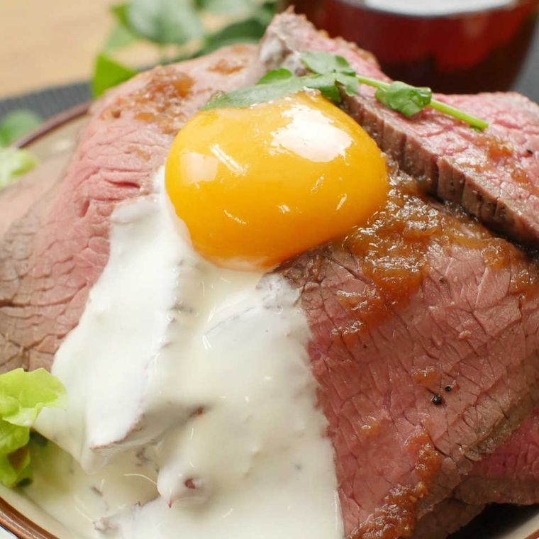 ローストビーフ丼の上に白いソースがかけられており、卵黄がトッピングされている