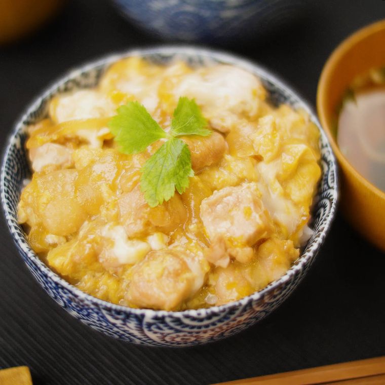 黒いお盆の上に、親子丼が入った藍染の丼が置かれ、その横には茶色いお椀に入った味噌汁が置かれている