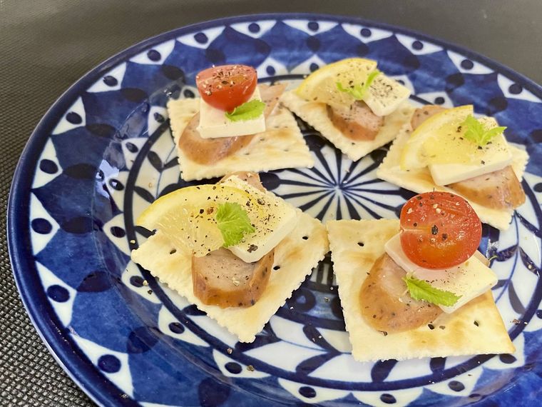 クラッカーの上にサラダチキンスティック スモークやサラダやチーズを盛り付けている