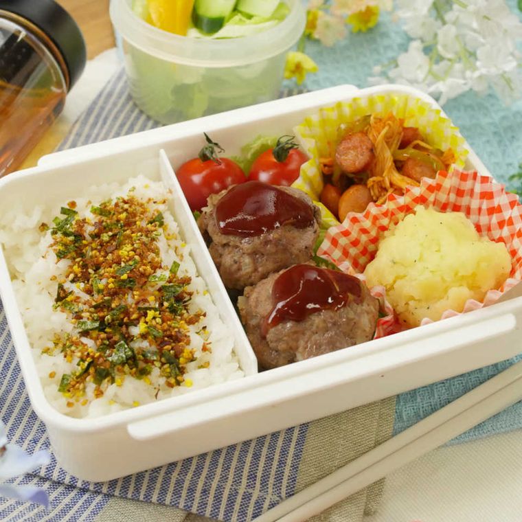 白い長方形の弁当箱に、ふりかけがかかったごはん、ハンバーグ、マッシュポテト、ナポリタン、ミニトマトが詰め込まれている