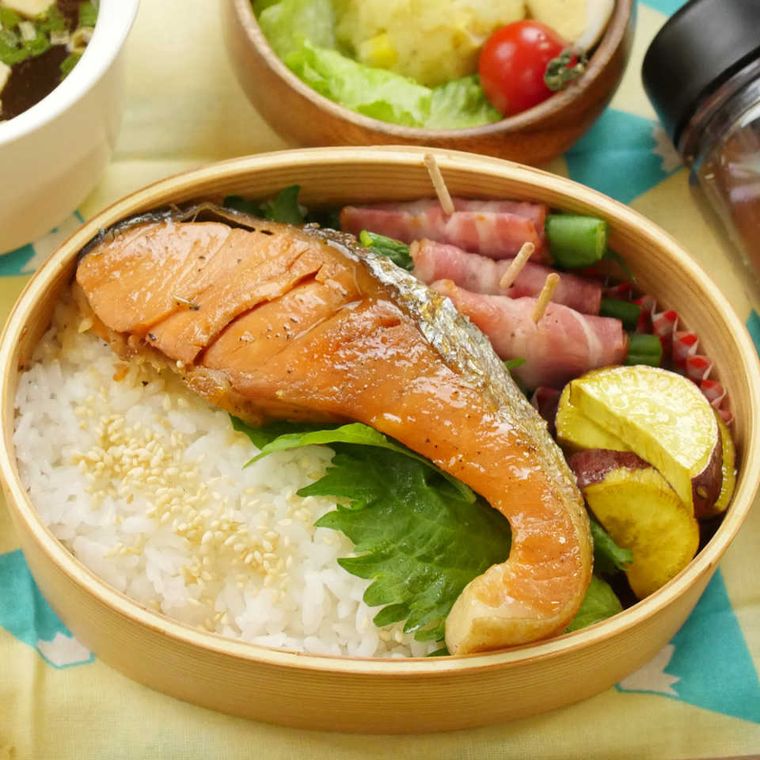 わっぱの弁当箱に、ごはん、焼き鮭、大葉、アスパラベーコン、さつまいものソテーなどが詰め込まれている