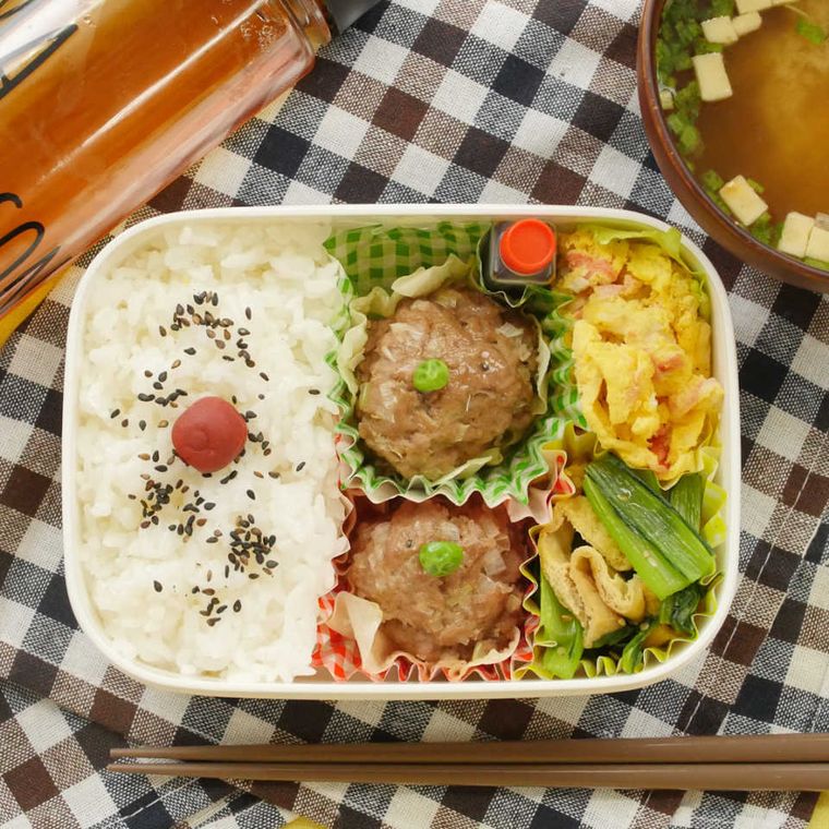 白い長方形の弁当箱に、梅干しとごまがのったごはん、シュウマイ、ポテトサラダ、小松菜と油揚げの煮物が詰め込まれている