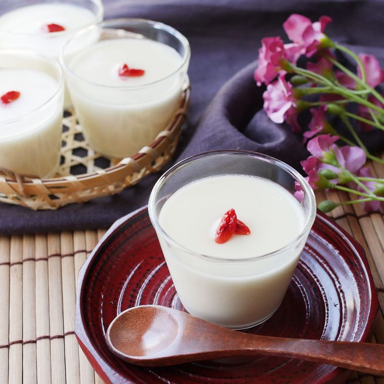 杏仁豆腐の入ったガラスの器が、茶色い茶托の上に置かれており、奥にも杏仁豆腐の入ったガラスの器が3つ並べられている