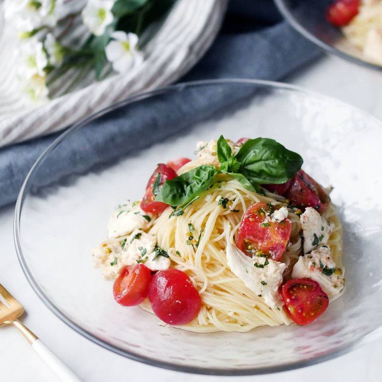 モッツァレラチーズ、ミニトマト、バジルが入りパスタが盛られたガラスの皿