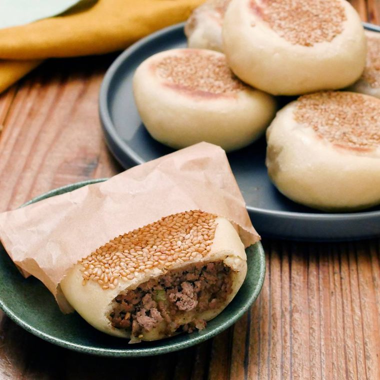 表面にごまがまぶされたひき肉入りのお焼きが、緑色の皿と紺色の皿にのせられており、木のテーブルの上に置かれている