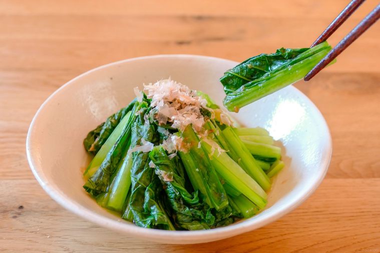 白い器に盛られている小松菜のおひたしを箸で持ち上げる様子