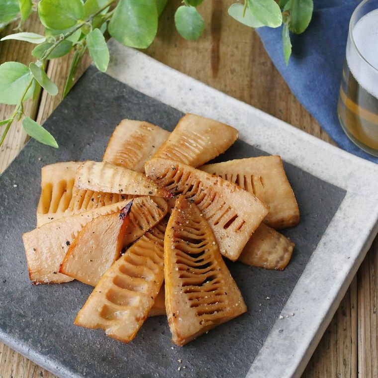 たけのこの炒め物が盛り付けられた灰色の皿が、木のテーブルの上に置かれている