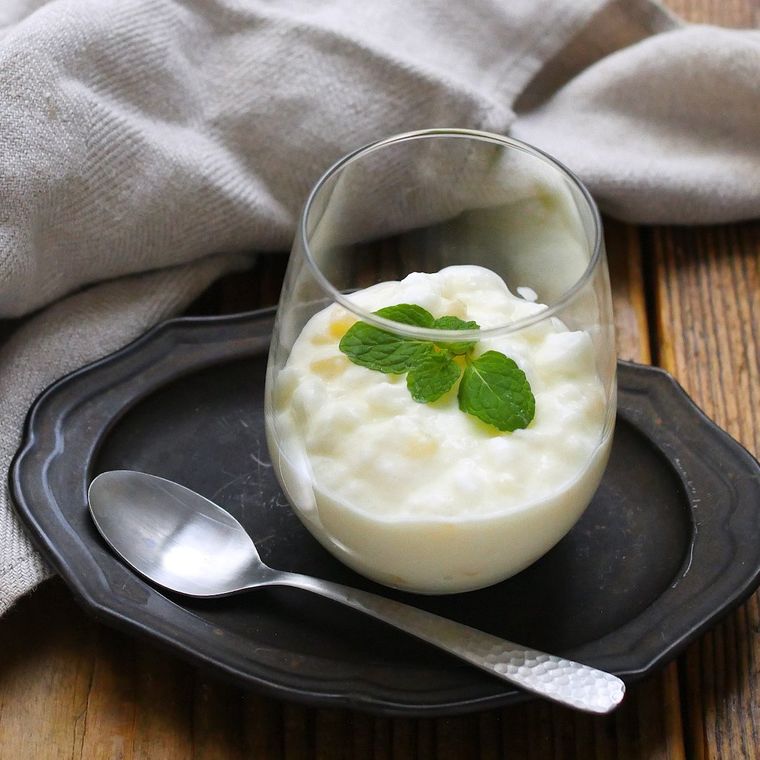 ヨーグルトとミントが入ったガラスの器が、黒い皿の上にスプーンと一緒に置かれており、奥には灰色の布が広げられている