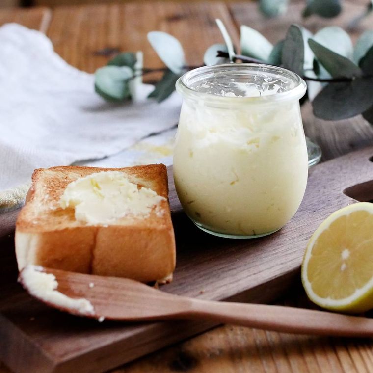 木のまな板の上に、バターが塗られた食パンと、バターが入った瓶と、バターナイフが置かれており、奥には白い布が広げられている