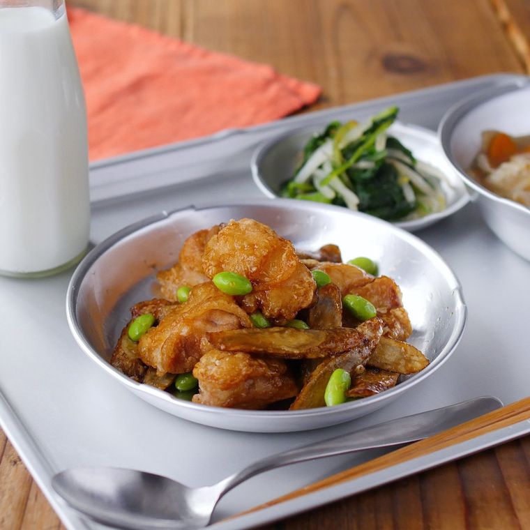 給食用のアルミトレーの上に、おかずが入ったアルミの食器3皿と、牛乳が入った瓶と、スプーンが並べられている様子