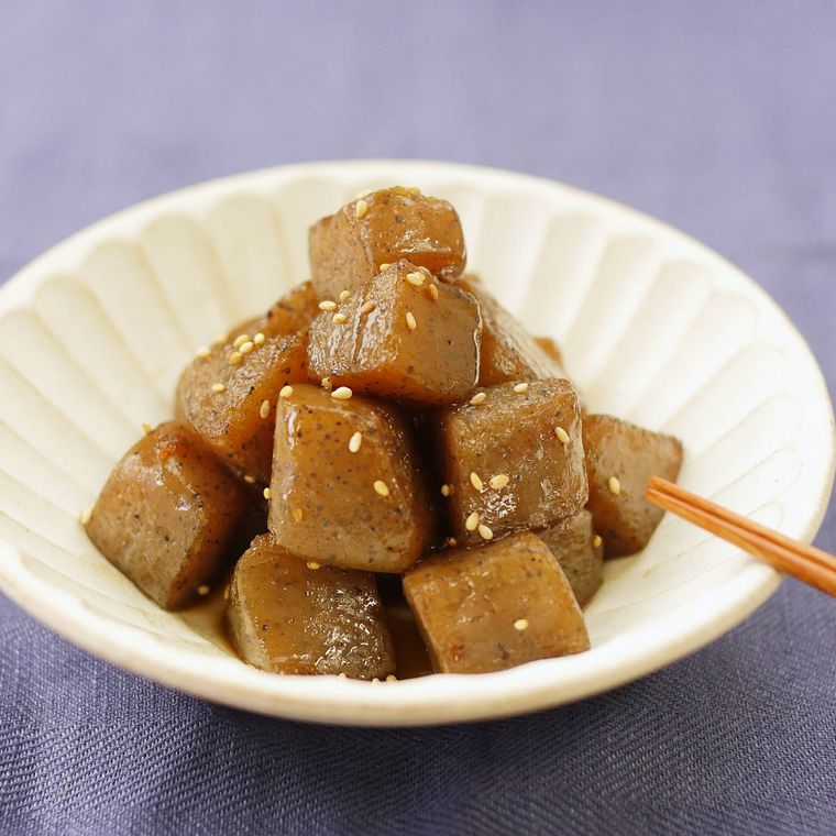 角切りこんにゃくの煮物が盛られた白い器が、紫色の布が敷かれたテーブルの上に置かれている