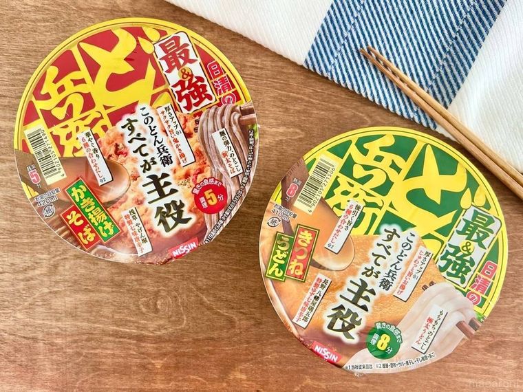 「最強どん兵衛」と書かれたカップ麺2個と、白地に青い模様が入った布と、木の箸が、木のテーブルの上に並べられている