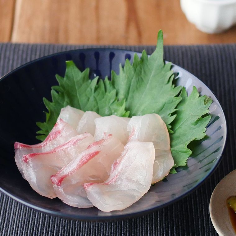 黒い丸皿に大葉と一緒に盛られた鯛の昆布締めが、机の上に置かれている