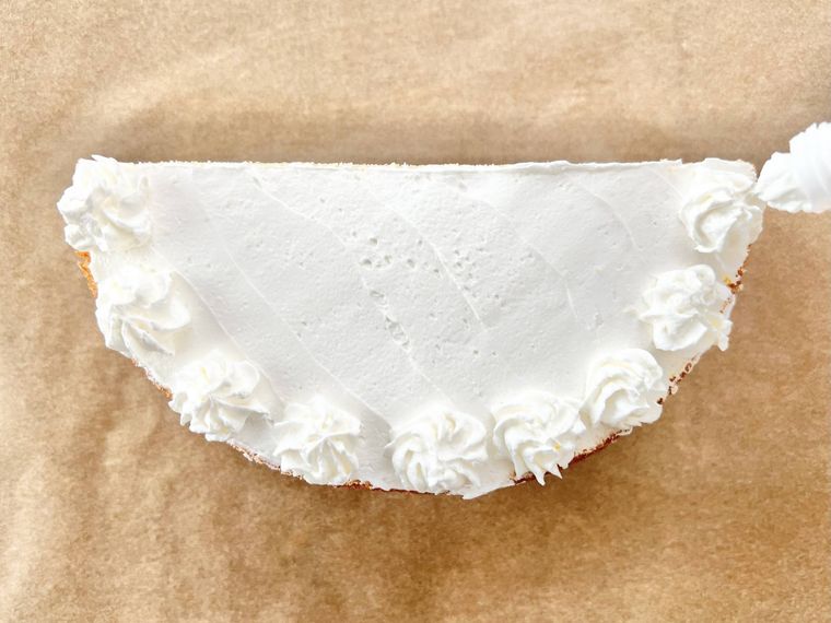 表面にホイップクリームが塗られた半月型のスポンジケーキに、ホイップクリームを絞り出してデコレーションをしている