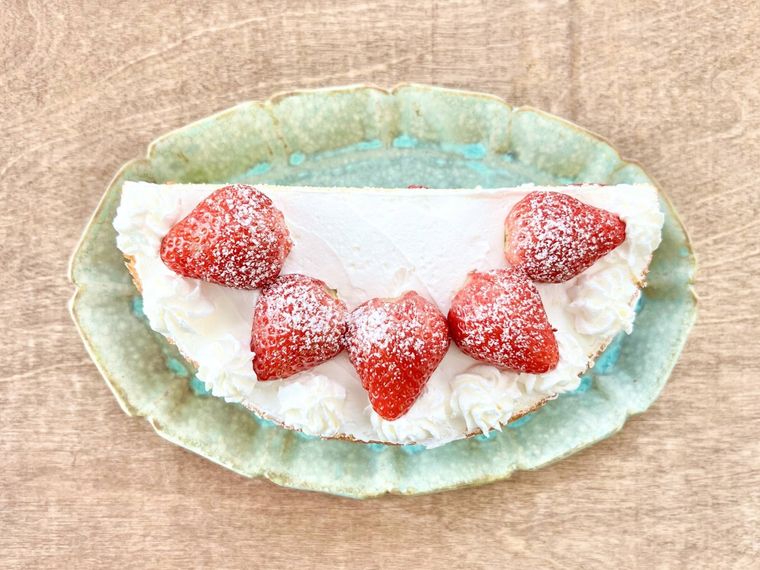 ホイップクリームとイチゴと粉砂糖でデコレーションされた半月型のスポンジケーキが、緑色の皿に盛り付けられている