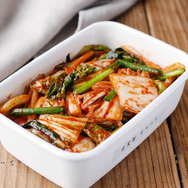 キムチが入った白いホーロー容器と灰色の布が、木のテーブルの上に置かれている