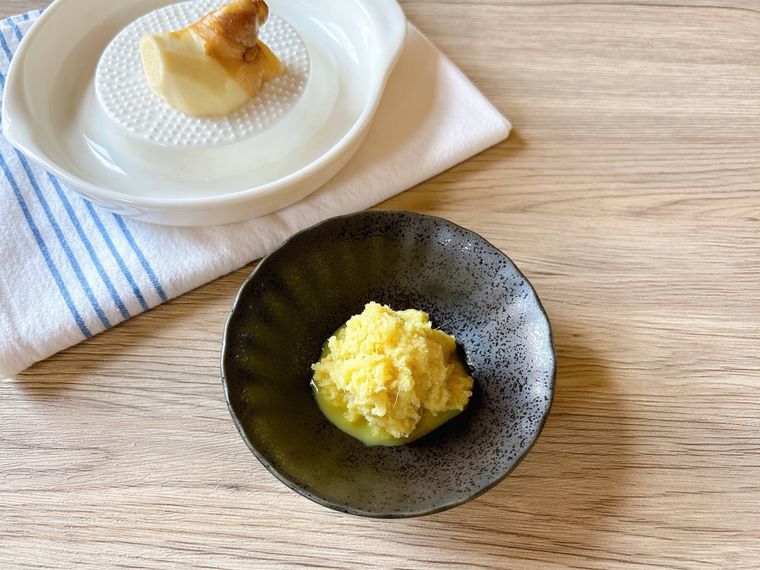 黒色の器に盛られたすりおろししょうが、しょうががおかれたおろし器