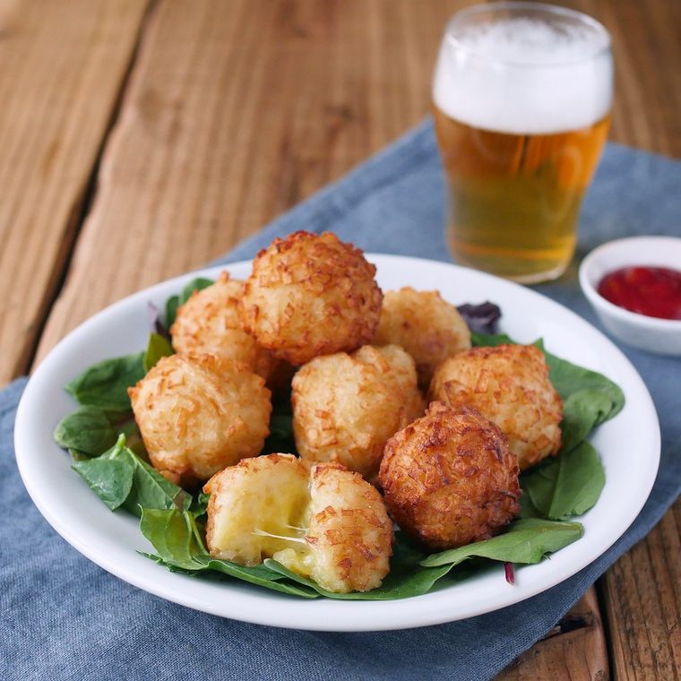 白い皿に盛られたじゃがチーズボール、ケチャップ、ビール入りのグラス