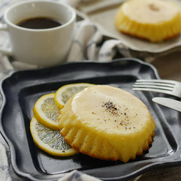 黒っぽい皿に盛られた濃厚チーズケーキマドレーヌ、コーヒーカップ