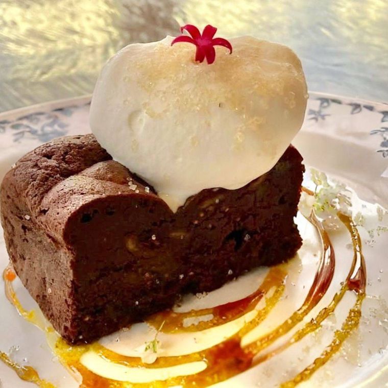 長方形のガトーショコラにぽってりとした生クリーム、エディブルフラワーがのっている