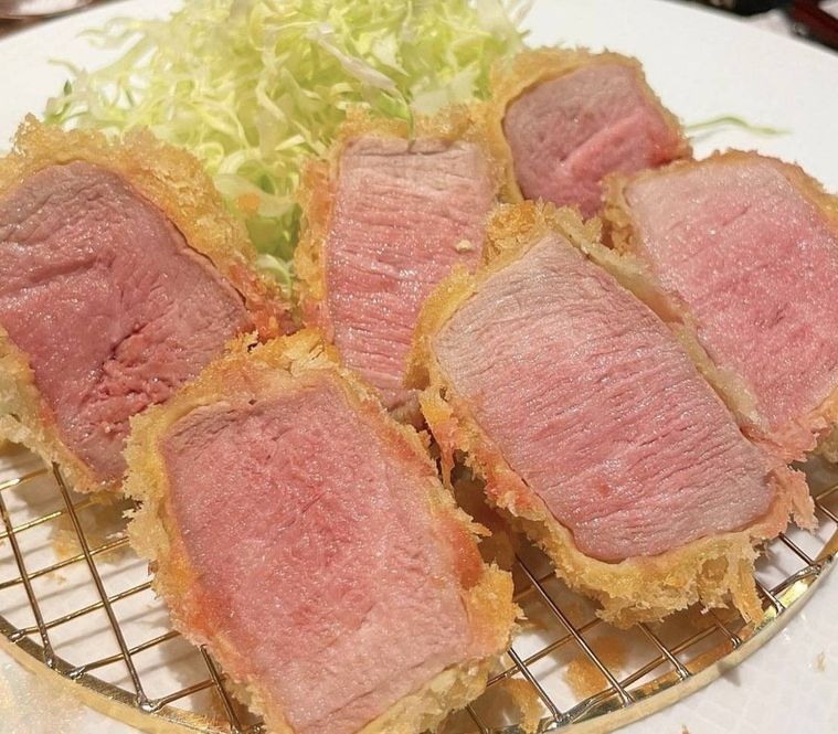 白いお皿に盛り付けられたピンク色したフィレ肉のカツレツと千切りキャベツ