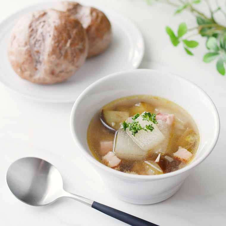 白い器に盛られた冬瓜となすとベーコンなどのスープと、2つの丸いパン