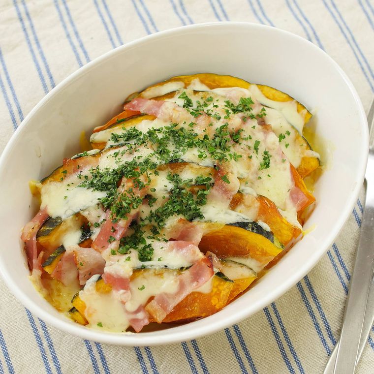 白いグラタン皿に盛られ、パセリをトッピングしたかぼちゃとベーコンのチーズ焼き