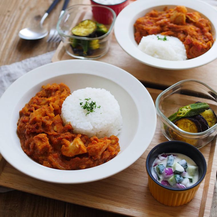 白い丸皿にバターチキンカレーが盛られ、横には小鉢に盛られた副菜が2種類置かれている