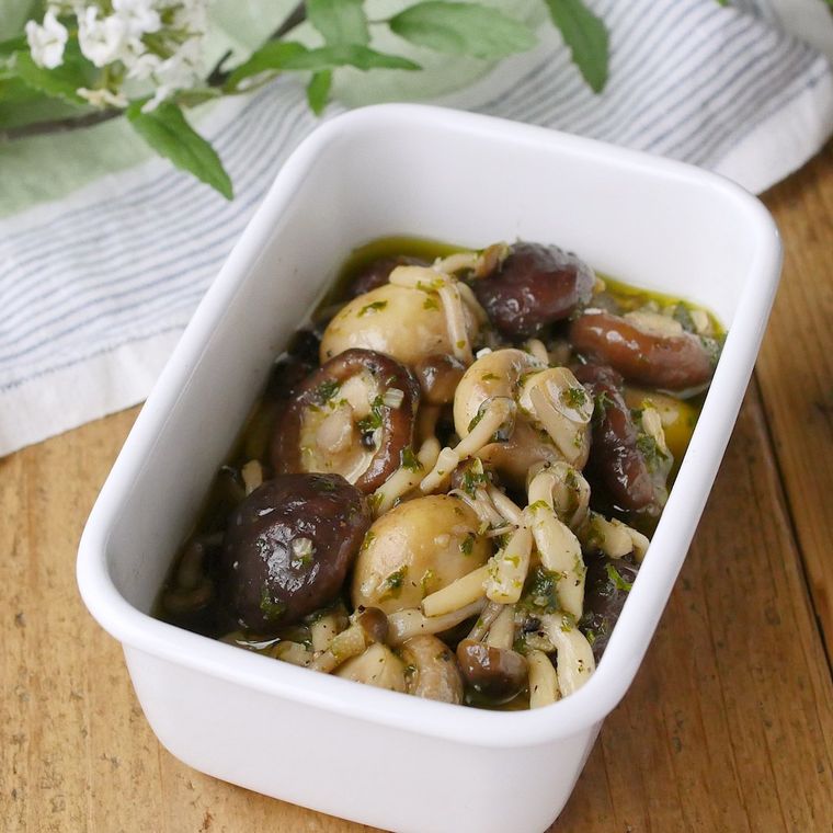 ホーロー容器に入ったマッシュルームのオイル蒸しの奥に植物が置かれている様子