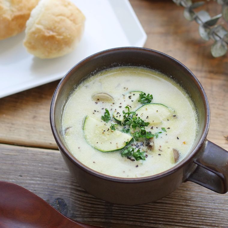 こげ茶のスープカップに鶏ひき肉とズッキーニの豆乳スープが盛られ、机の上に置かれている